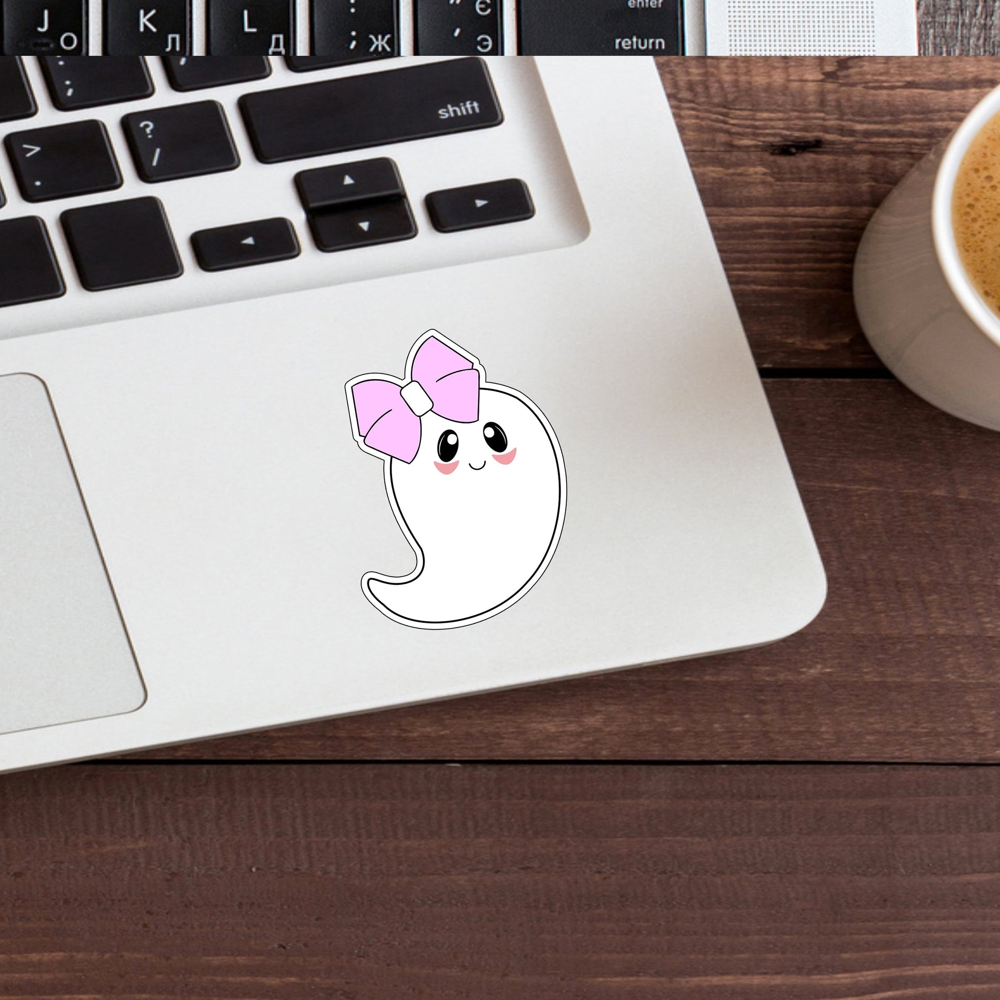 a cup of coffee next to a laptop with a sticker of a ghost