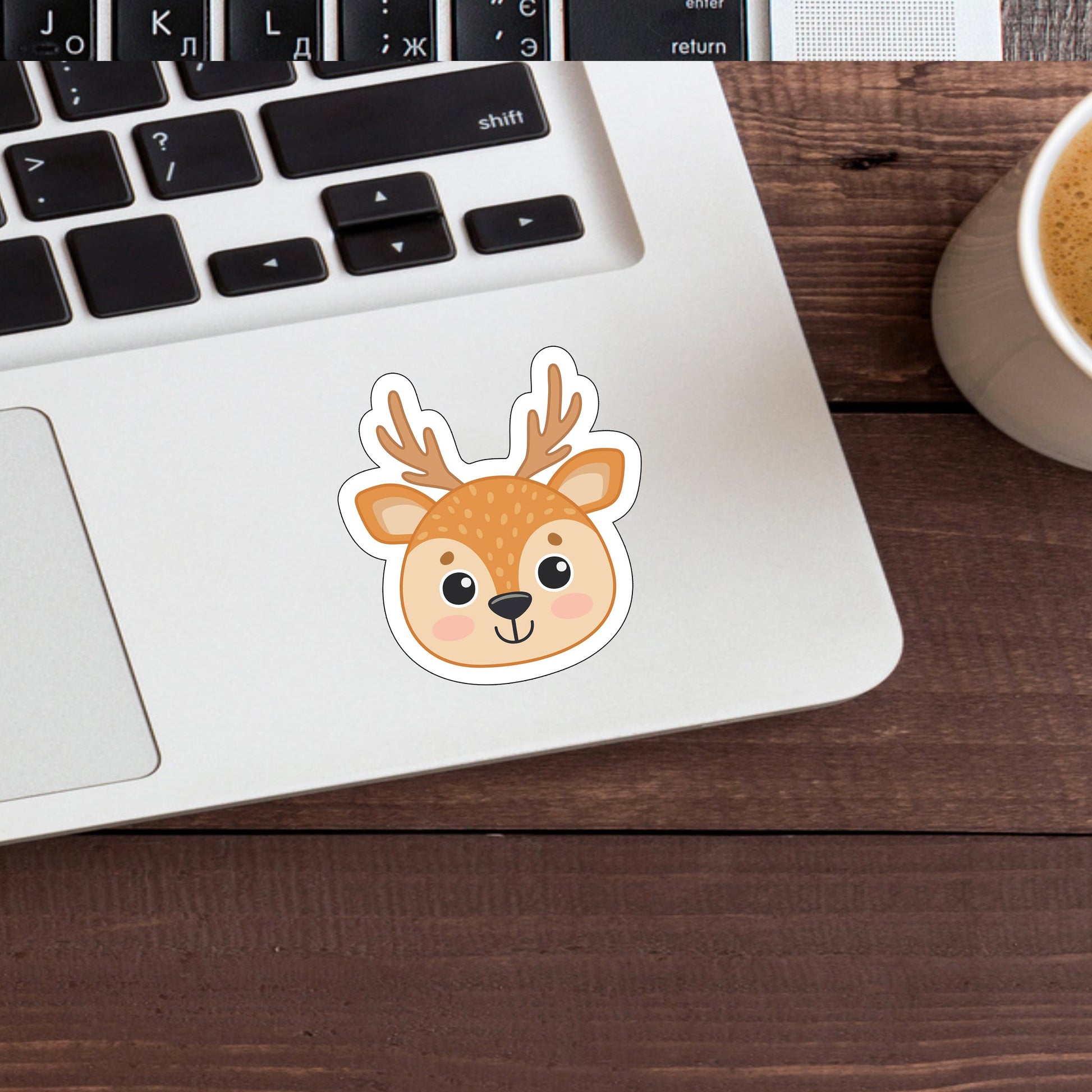 a cup of coffee next to a laptop with a sticker of a deer