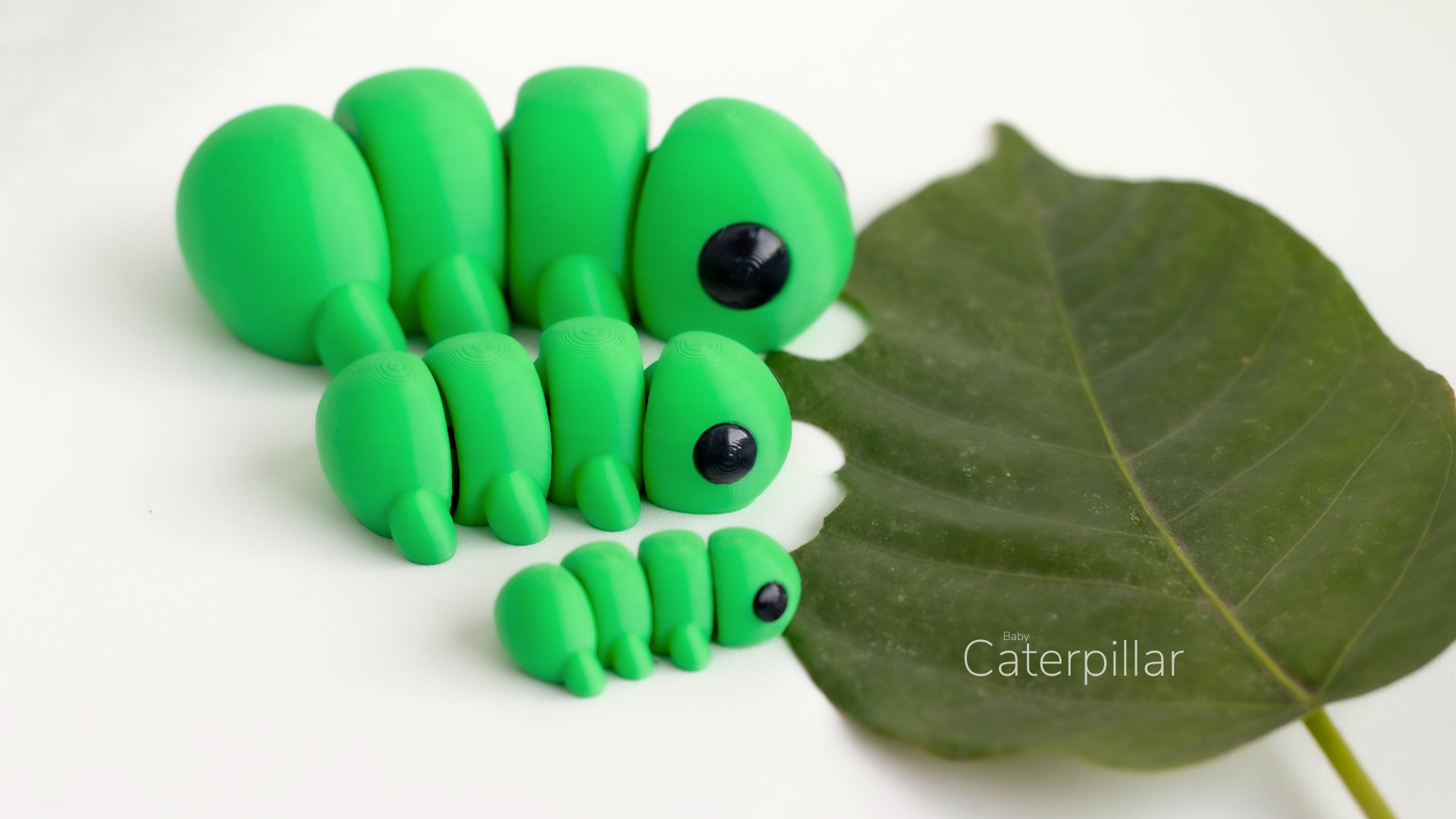 a close up of a green toy caterpillar next to a leaf