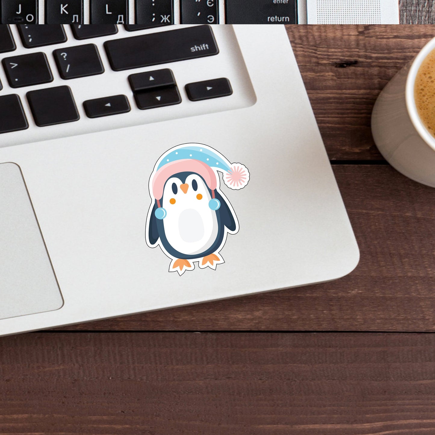 a penguin sticker on a laptop next to a cup of coffee