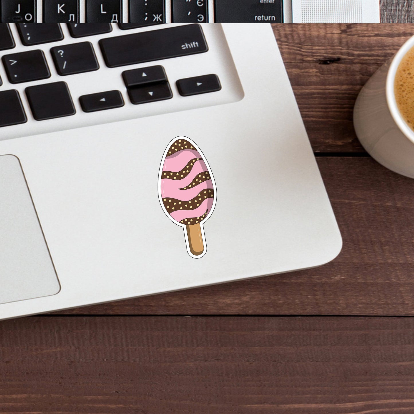 a cup of coffee next to a laptop with a sticker of an ice cream