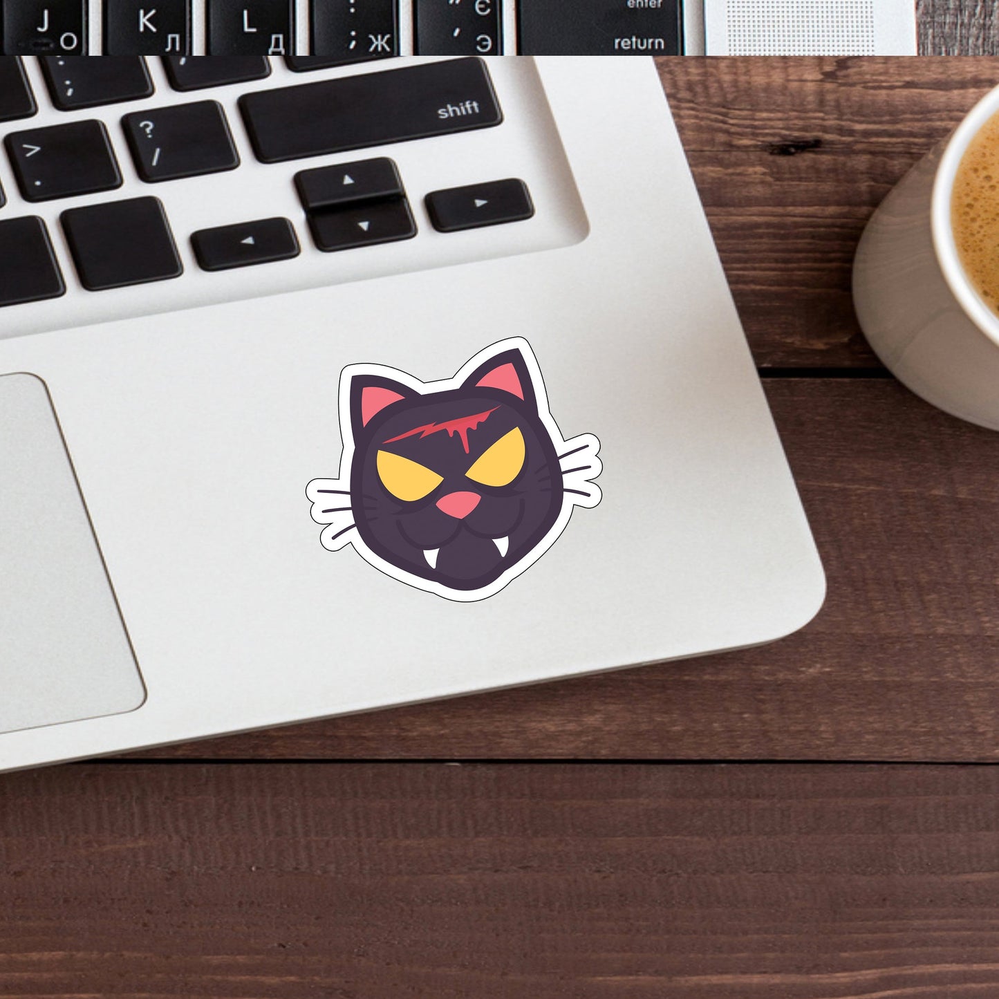 a cup of coffee next to a laptop with a sticker of a black cat