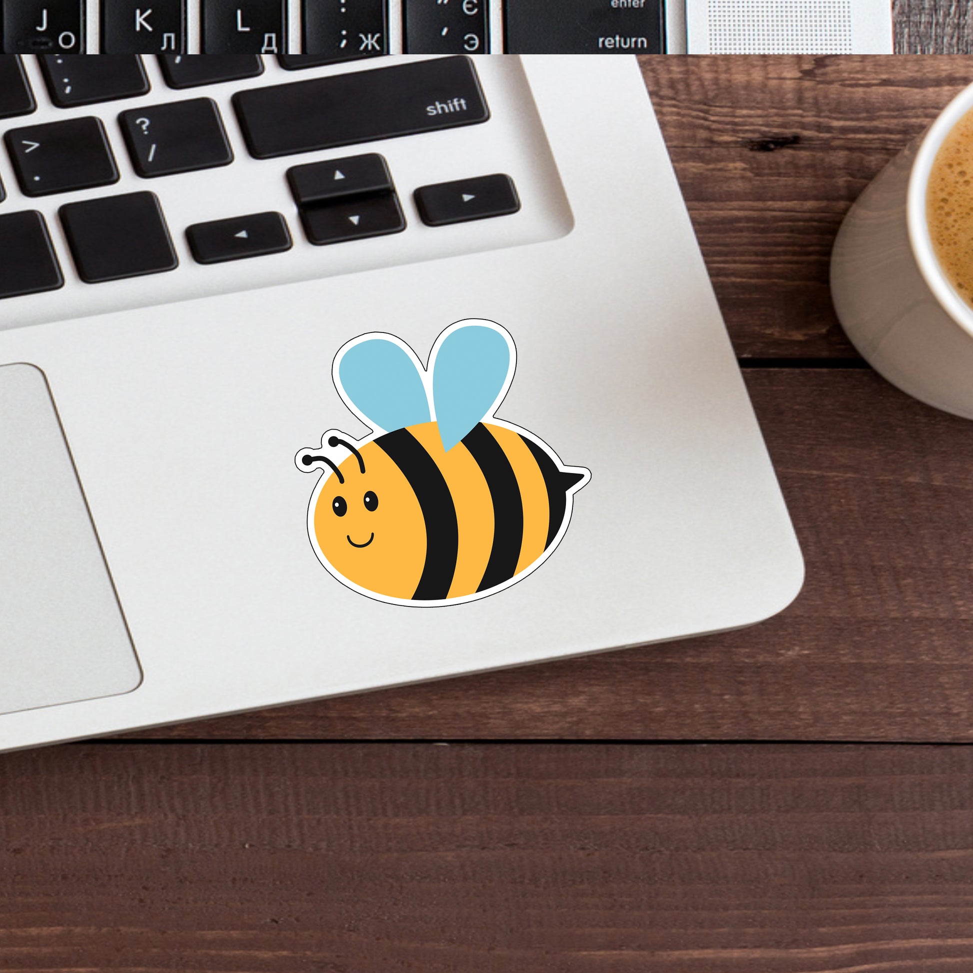 a cup of coffee next to a laptop with a sticker of a bee on