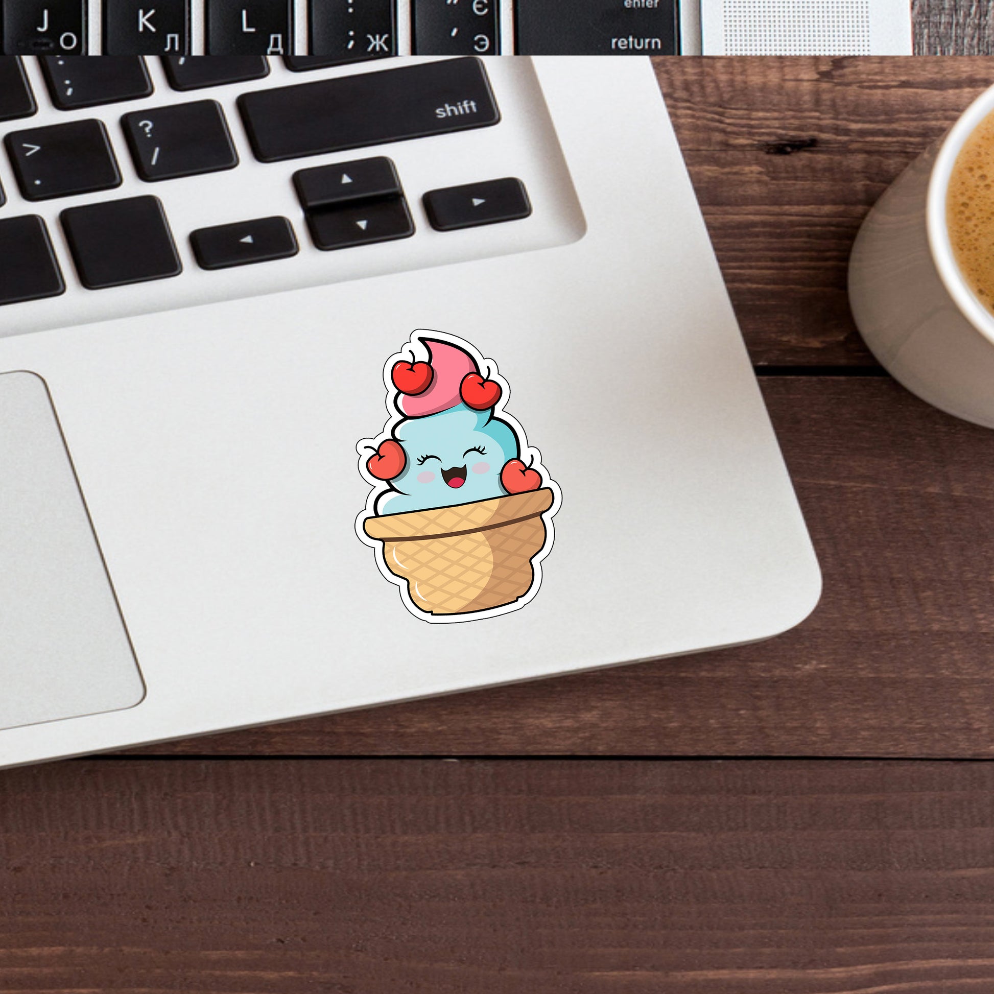 a cup of coffee next to a laptop with a sticker of an ice cream